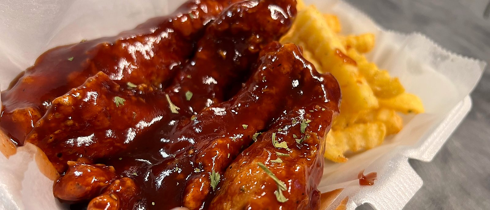 Glossy BBQ chicken tenders beside seasoned crinkle fries