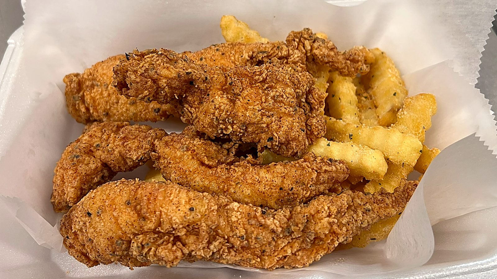 Golden hand breaded chicken tenders over seasoned crinkle fries